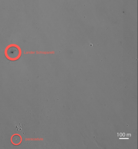 Il cratere nero provocato sulla superficie di Marte dal violento impatto del Lander Schiaparelli, pesante 500 chili, precipitato a 300 chilometri orari. In basso il paracadute, chiaro, atterrato più a sud