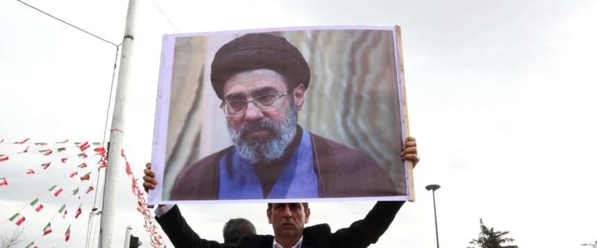 Un manifestante mostra la foto del figlio di Khamenei, Mojtaba, eletto nuova Guida suprema dell’Iran